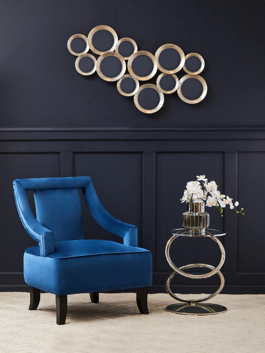 Blue velvet accent chair next to chrome glass side table and gold circle wall art