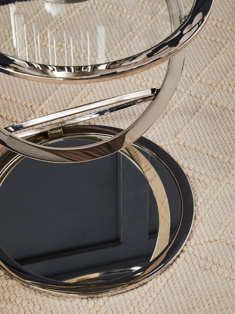 Glass and chrome side table with circular mirrored base on textured beige rug
