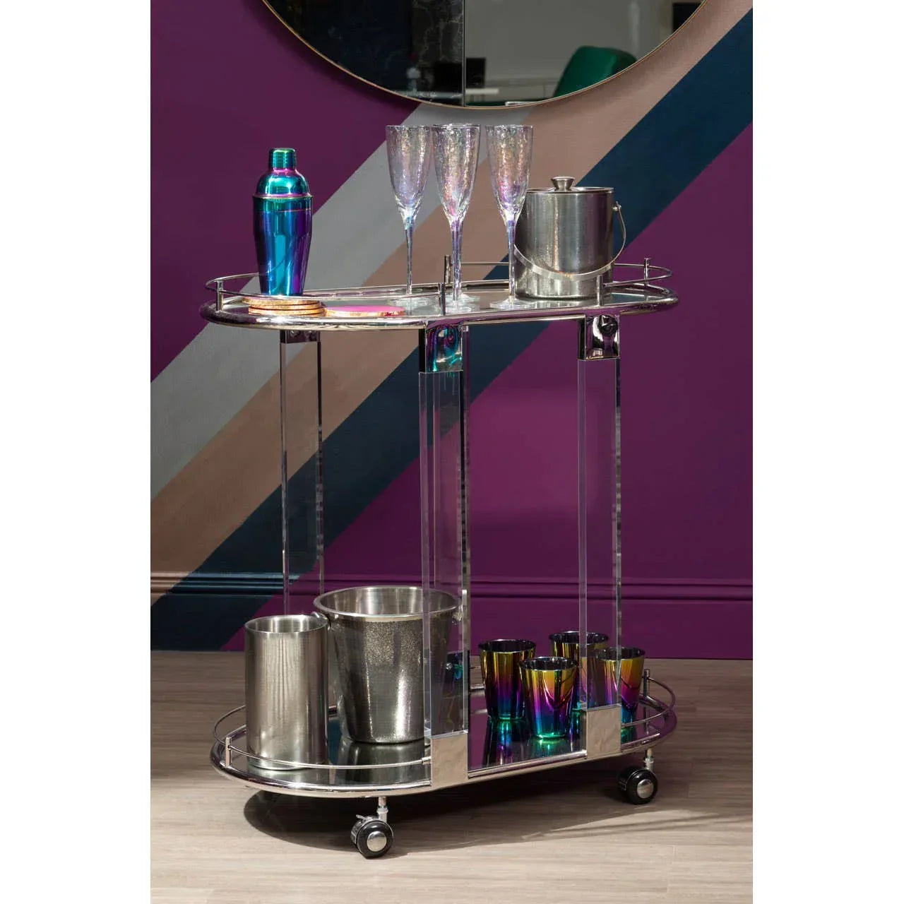 Chrome and acrylic drinks trolley with glassware and cocktail accessories against purple wall