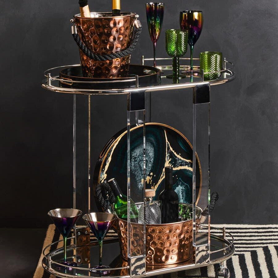 Chrome and copper drinks trolley with wine, glasses, and bar accessories on striped rug