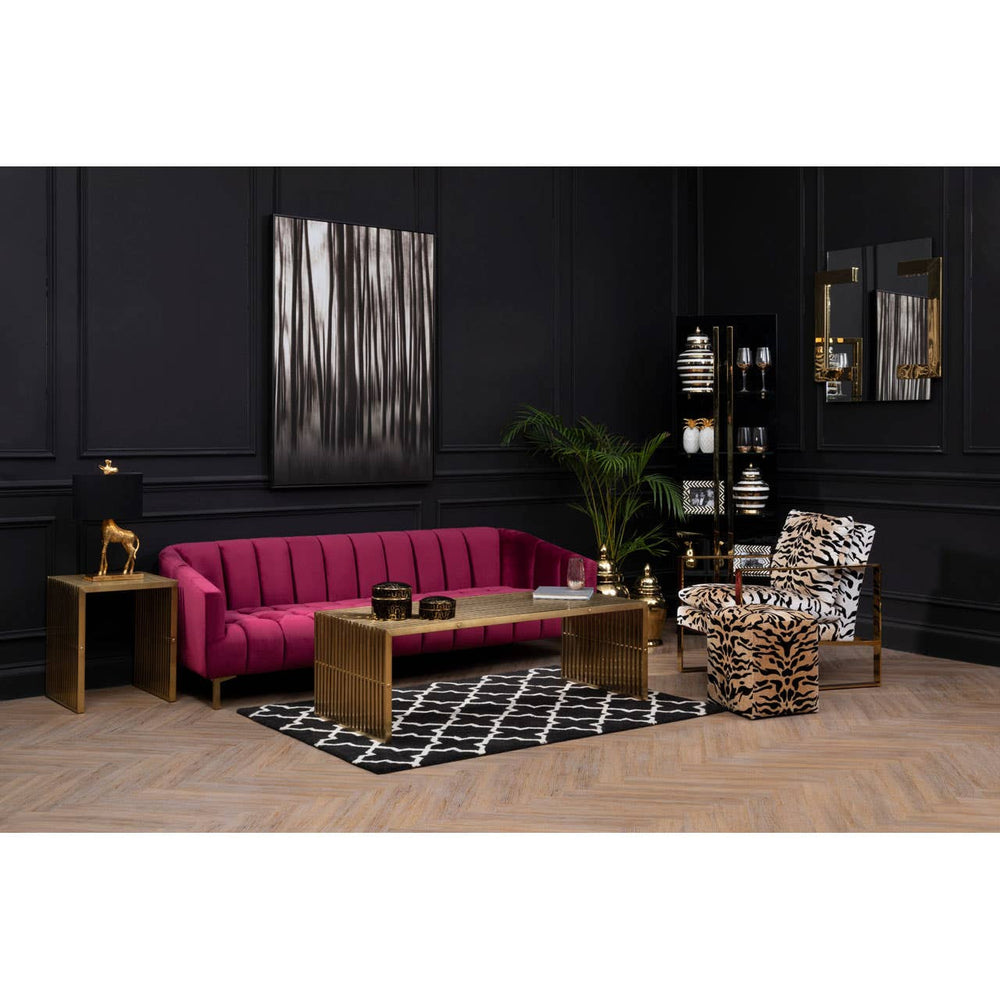 A luxurious three-seat sofa upholstered in rich wine-colored velvet, featuring a tufted backrest and elegant armrests. The sofa is positioned in a stylish living room setting with dark walls, a patterned black and white rug, a wooden coffee table, and decorative accessories, including a plant and artwork on the walls