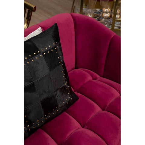 A close-up view of a luxurious wine-colored velvet sofa featuring a tufted design, with a decorative black pillow adorned with gold studs placed on the seat. The background suggests a stylish interior setting