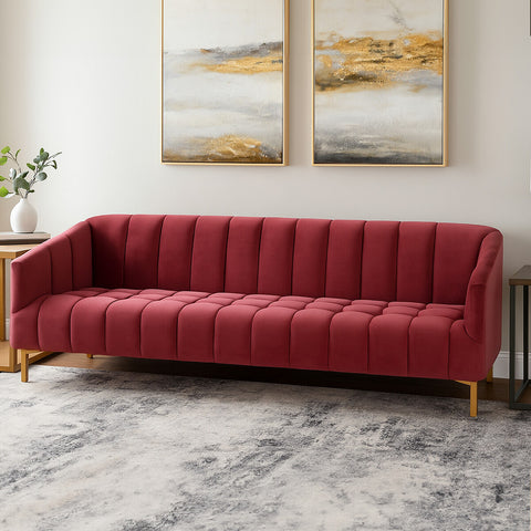 A three-seat sofa upholstered in rich wine-colored velvet, featuring a tufted design and sleek wooden legs. The sofa is positioned in a modern living space with abstract artwork on the wall and a light-colored rug underneath