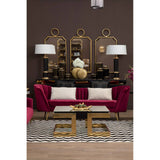 A luxurious three-seat sofa upholstered in rich wine-colored velvet, featuring elegant curved arms and plush cushions. The sofa is positioned in a stylish living room setting with a dark brown wall, complemented by a decorative gold-framed mirror and matching lamps on either side. A modern coffee table with a gold base sits in front of the sofa, resting on a patterned area rug