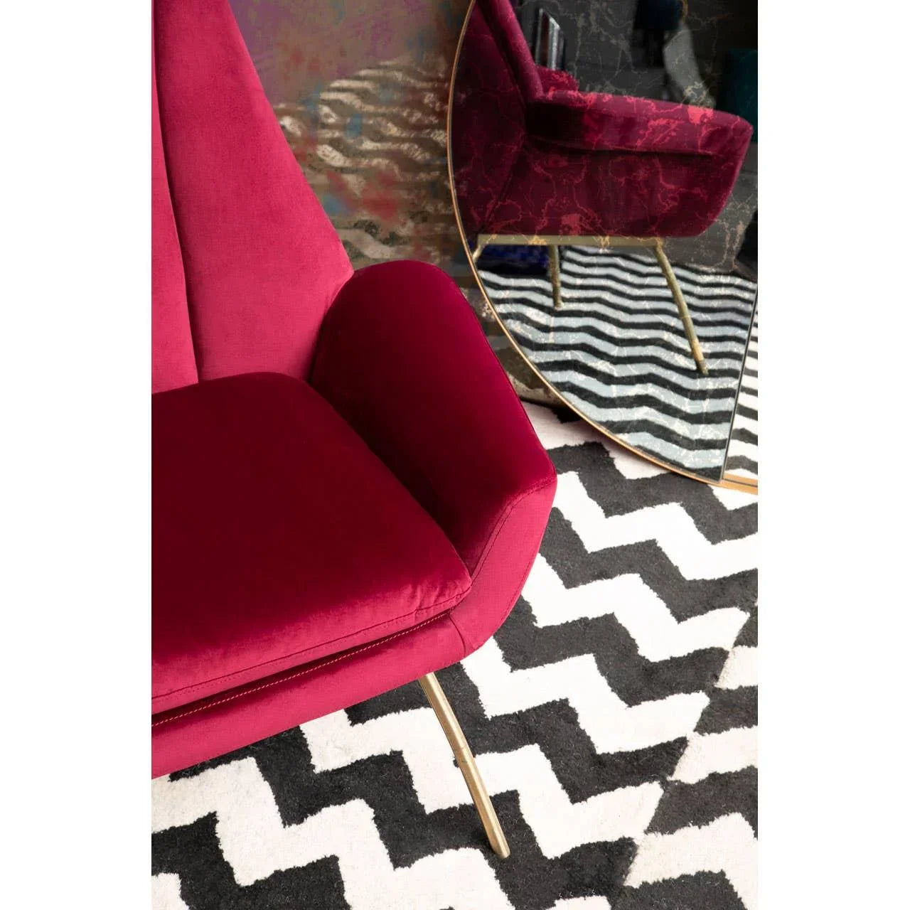 Red velvet accent chair with gold legs on black and white zigzag rug near mirror