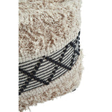 A close-up view of a shaggy pouffe featuring a textured cream-colored surface with black geometric patterns woven into the design. The pouffe has a soft, fluffy appearance, highlighting its cozy and stylish look, suitable for home decor