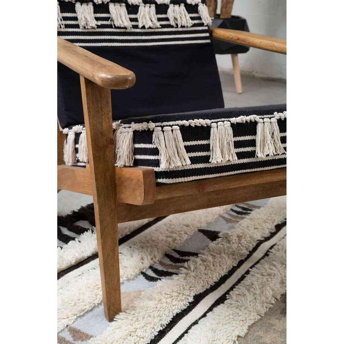 Wooden armchair with black and cream striped woven seat and tassels on patterned rug