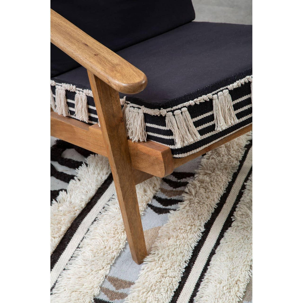 Wooden armchair with navy cushion and striped fringe detail on geometric patterned rug