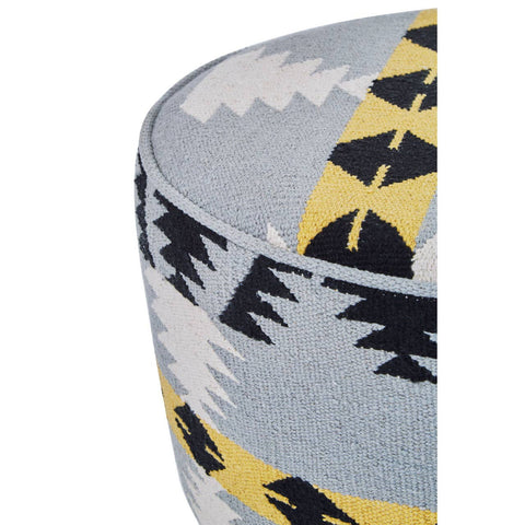 Round footstool featuring a colorful Kilim-style fabric with geometric patterns in shades of blue, yellow, and black, supported by sturdy mango wood legs. The design showcases a textured surface and a contemporary aesthetic suitable for home decor