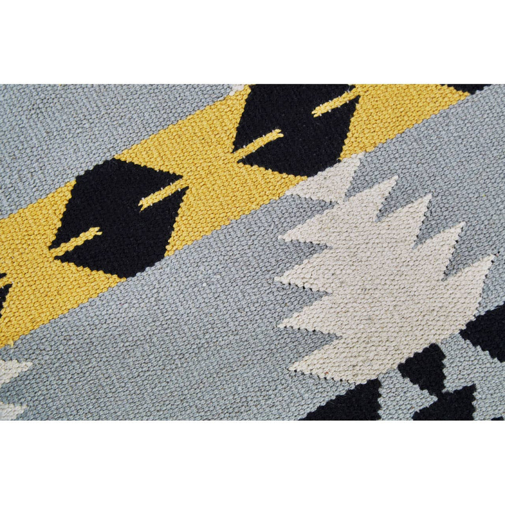 Round footstool featuring a colorful Kilim-style fabric with geometric patterns in shades of blue, yellow, black, and cream, supported by sturdy mango wood legs