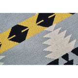 Round footstool featuring a colorful Kilim-style fabric with geometric patterns in shades of blue, yellow, black, and cream, supported by sturdy mango wood legs