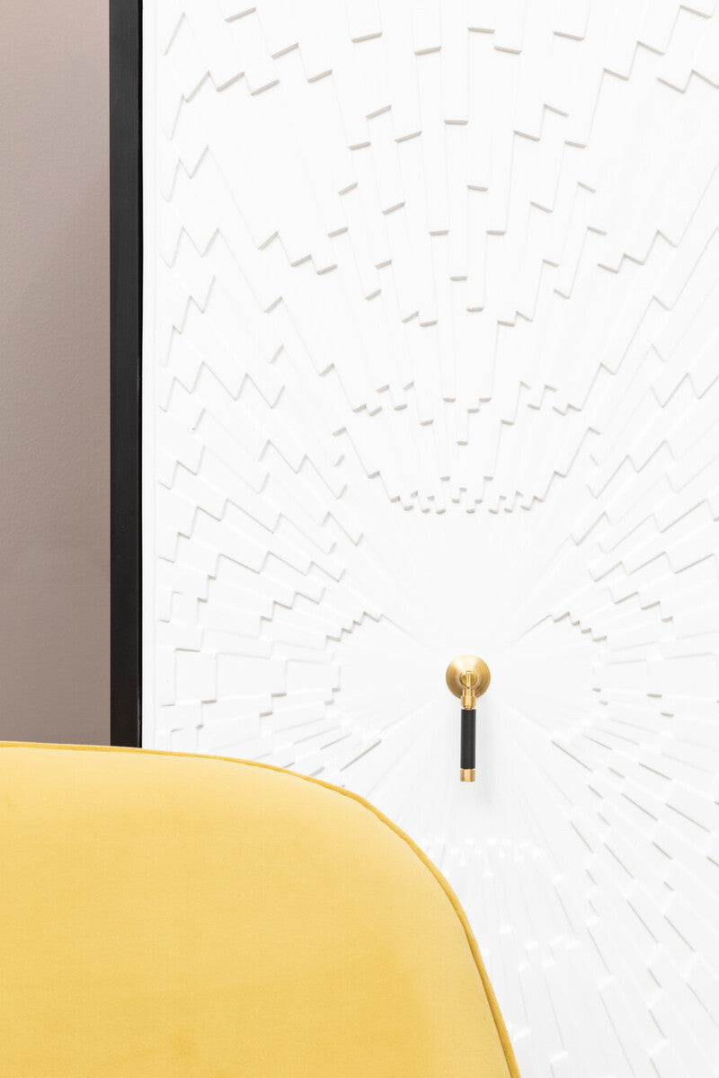 A close-up view of the Dumas Black and White Two Door Cabinet, featuring a textured white door with a gold handle, set against a light-colored wall. A portion of a yellow cushion is visible in the foreground, adding a pop of color to the scene