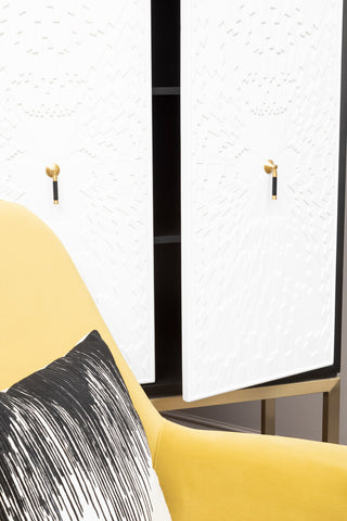 A stylish black and white two-door cabinet featuring sleek white doors with gold handles, positioned next to a yellow accent chair with a decorative black and white pillow. The cabinet has a modern design and is set against a neutral background
