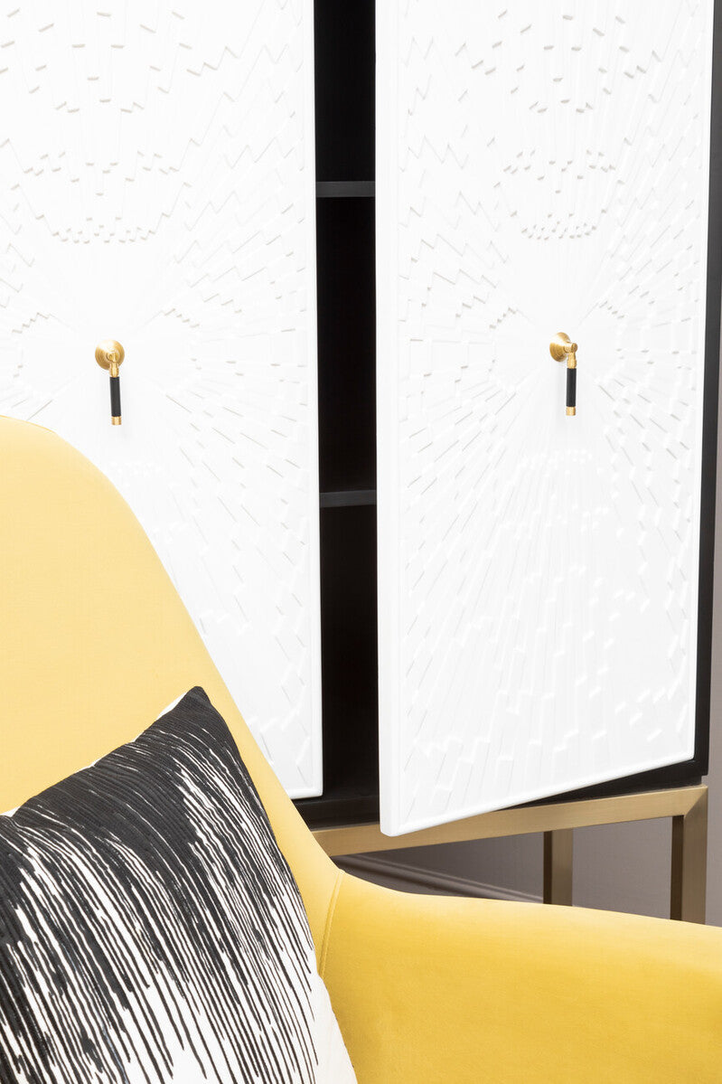 A stylish black and white two-door cabinet featuring sleek white doors with gold handles, positioned next to a yellow accent chair with a decorative black and white pillow. The cabinet has a modern design and is set against a neutral background