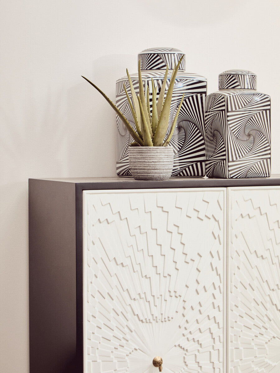 A stylish two-door cabinet featuring a textured white front and a dark wood frame, topped with three decorative vases in varying sizes, including a round pot with a green plant, set against a light-colored wall