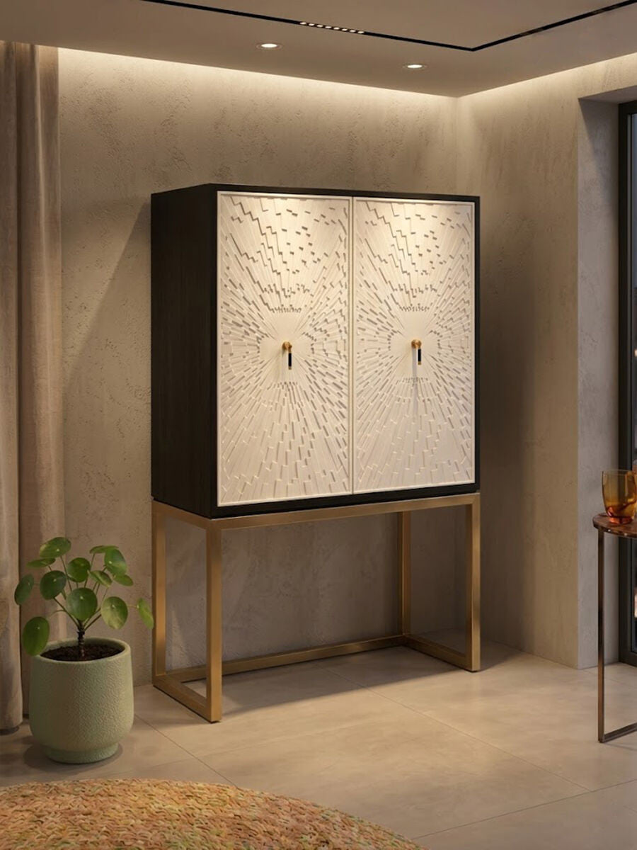 A stylish two-door cabinet featuring a black frame and white doors with intricate designs, set on a sleek gold metal base. The cabinet is positioned against a softly lit wall, with a potted plant nearby, creating a modern and elegant home decor setting