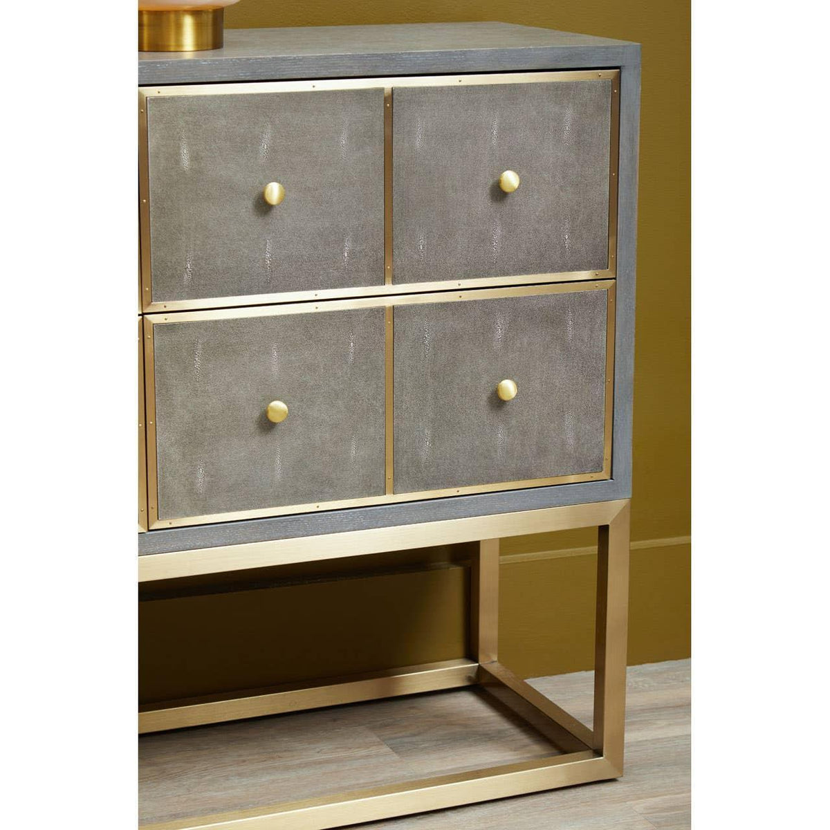 Grey and gold four drawer chest with brass knobs and metal frame on wood floor