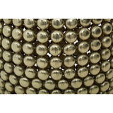 Close-up view of a gold finish stool and side table featuring a textured surface made up of small, round metallic beads arranged in a pattern. The overall design is sleek and modern, showcasing a shiny gold color that reflects light