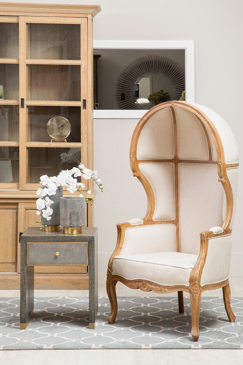 Beige canopy armchair with wood frame beside modern grey side table and display cabinet