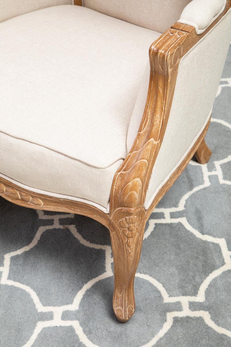 Carved wooden armchair with beige upholstery on patterned rug