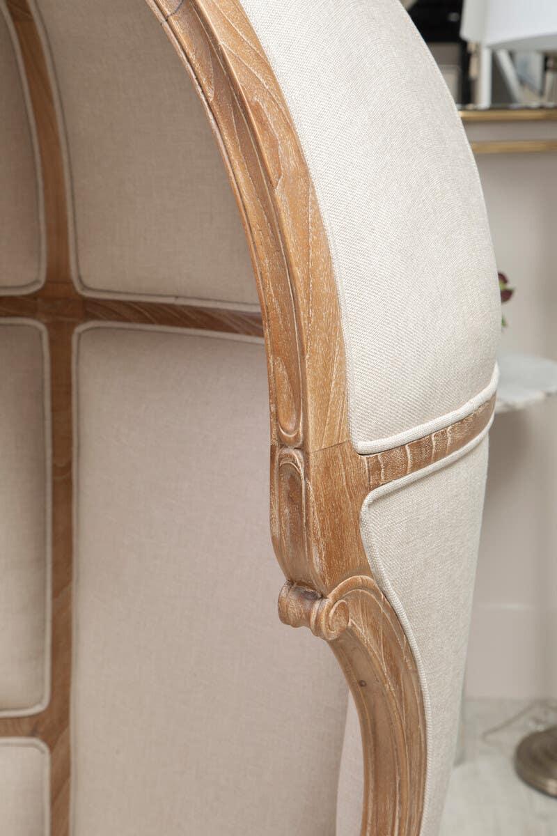 Closeup of beige upholstered accent chair with carved wooden frame detailing