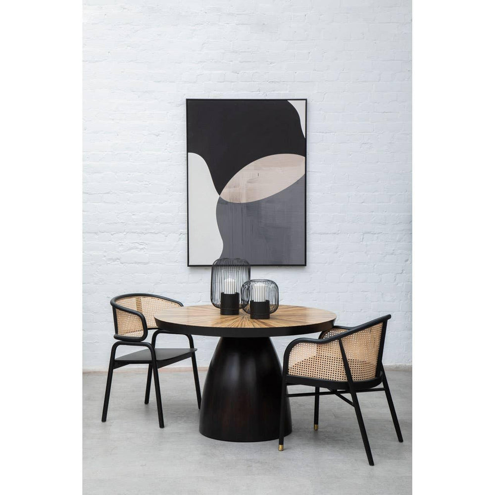 Round wood dining table with black base and two rattan chairs in modern dining room