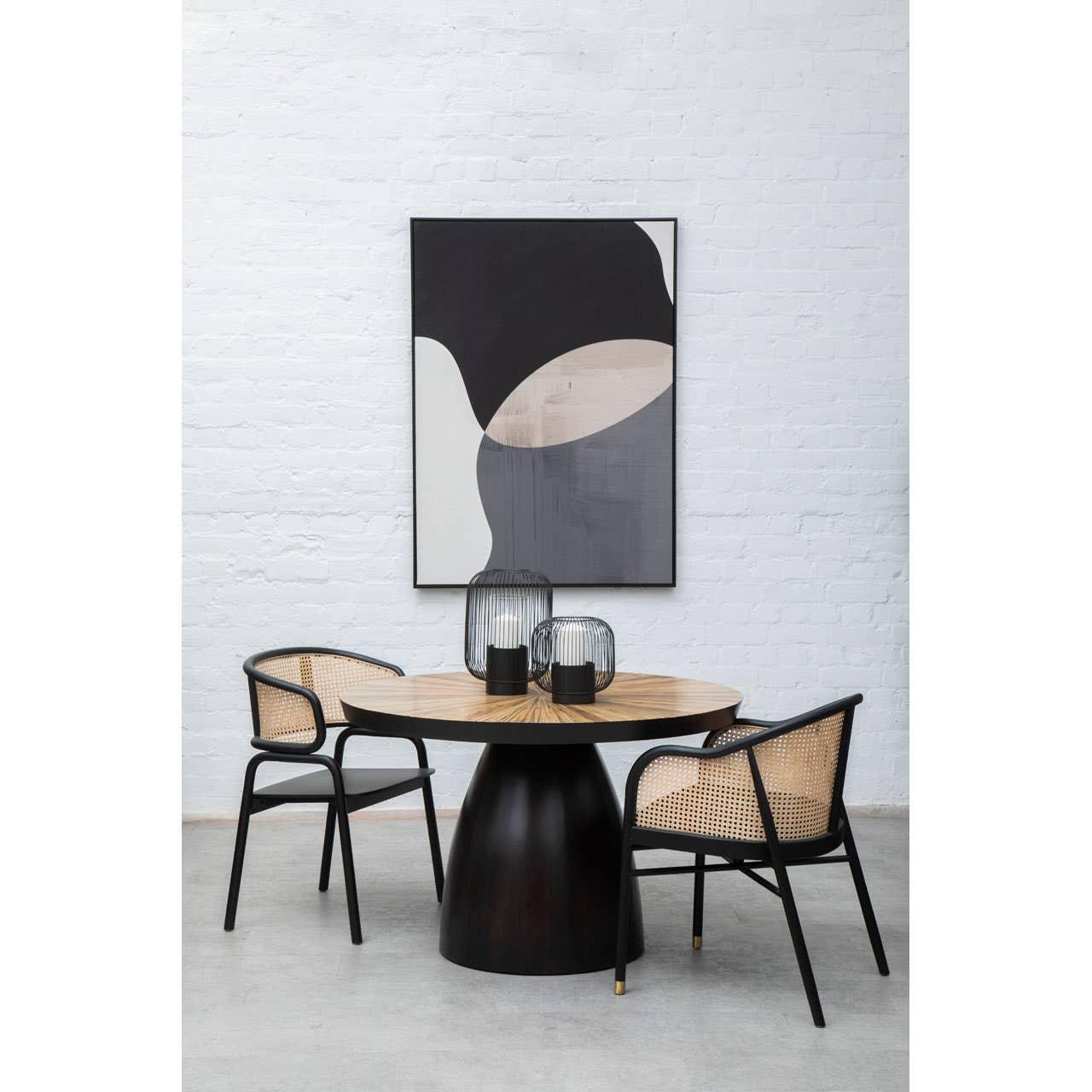 Round wood dining table with black base and two rattan chairs in modern dining room