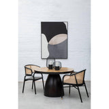 Round wood dining table with black base and two rattan chairs in modern dining room