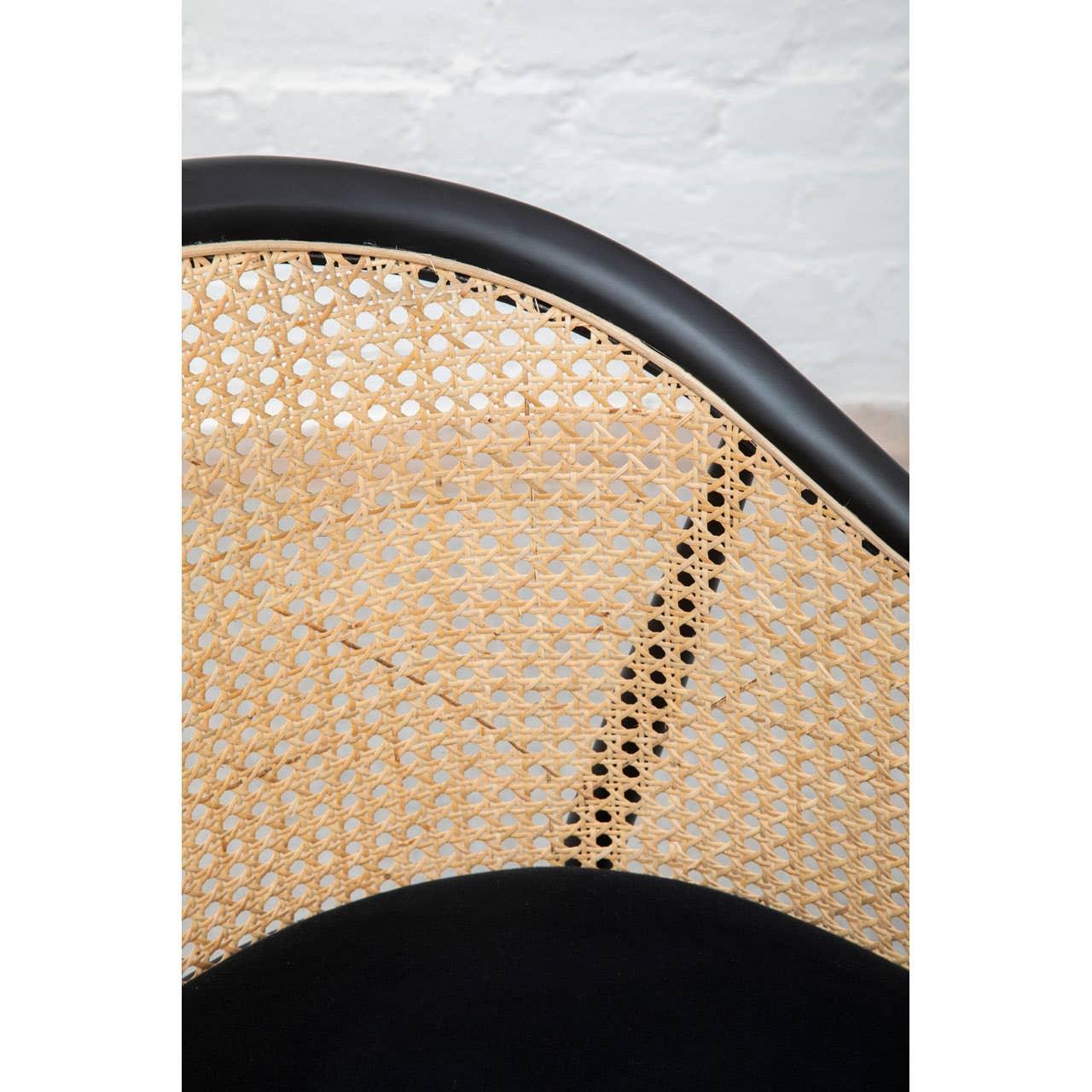 Closeup of rattan dining chair back with black frame against white brick wall