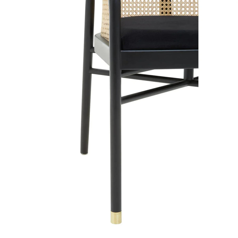 Black dining chair with cane backrest, gold-tipped leg and padded seat, side view