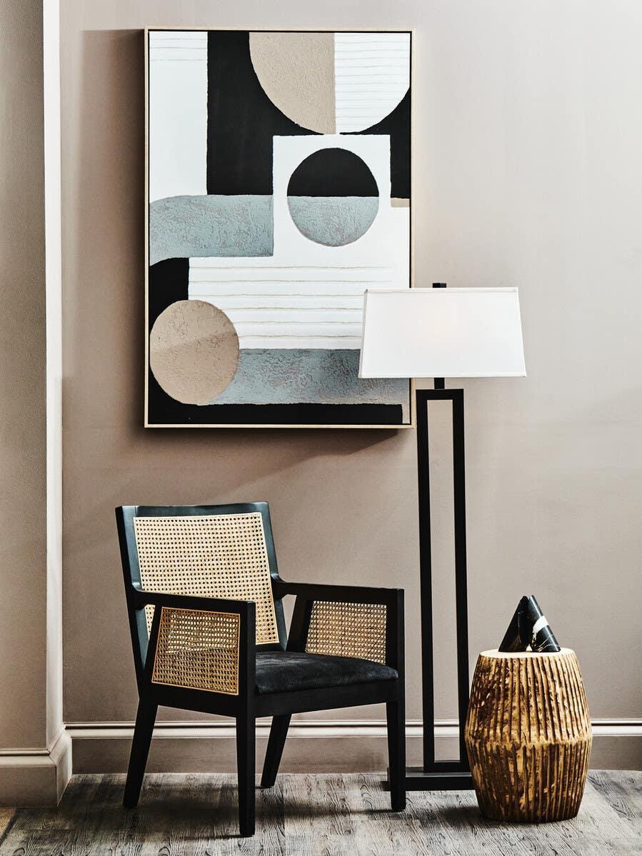Black wooden accent chair with rattan panels beside modern floor lamp and abstract wall art