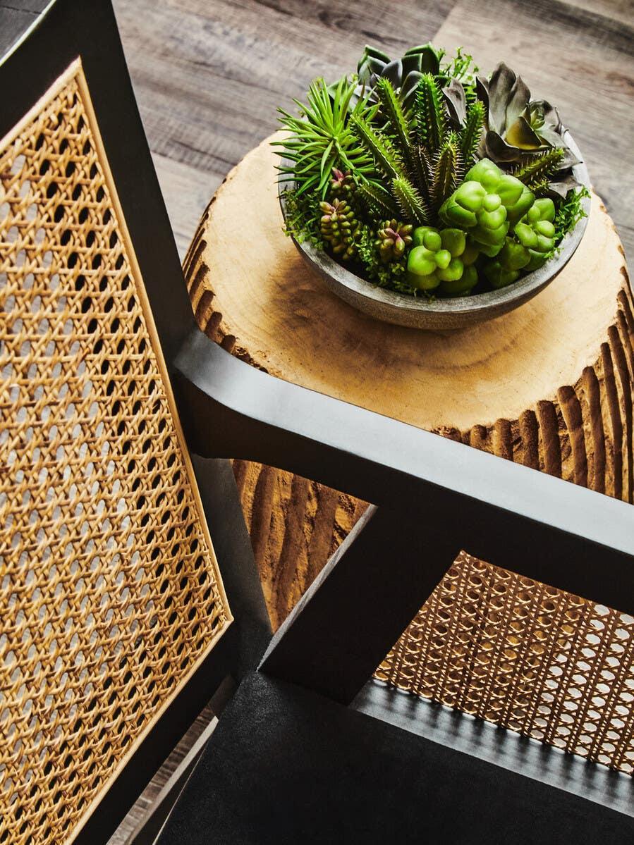 Rattan dining chair with black frame beside wooden table topped with bowl of artificial succulents