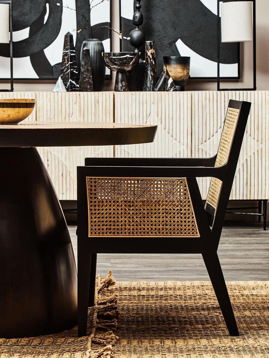 Black dining chair with rattan seat and backrest beside round wooden dining table