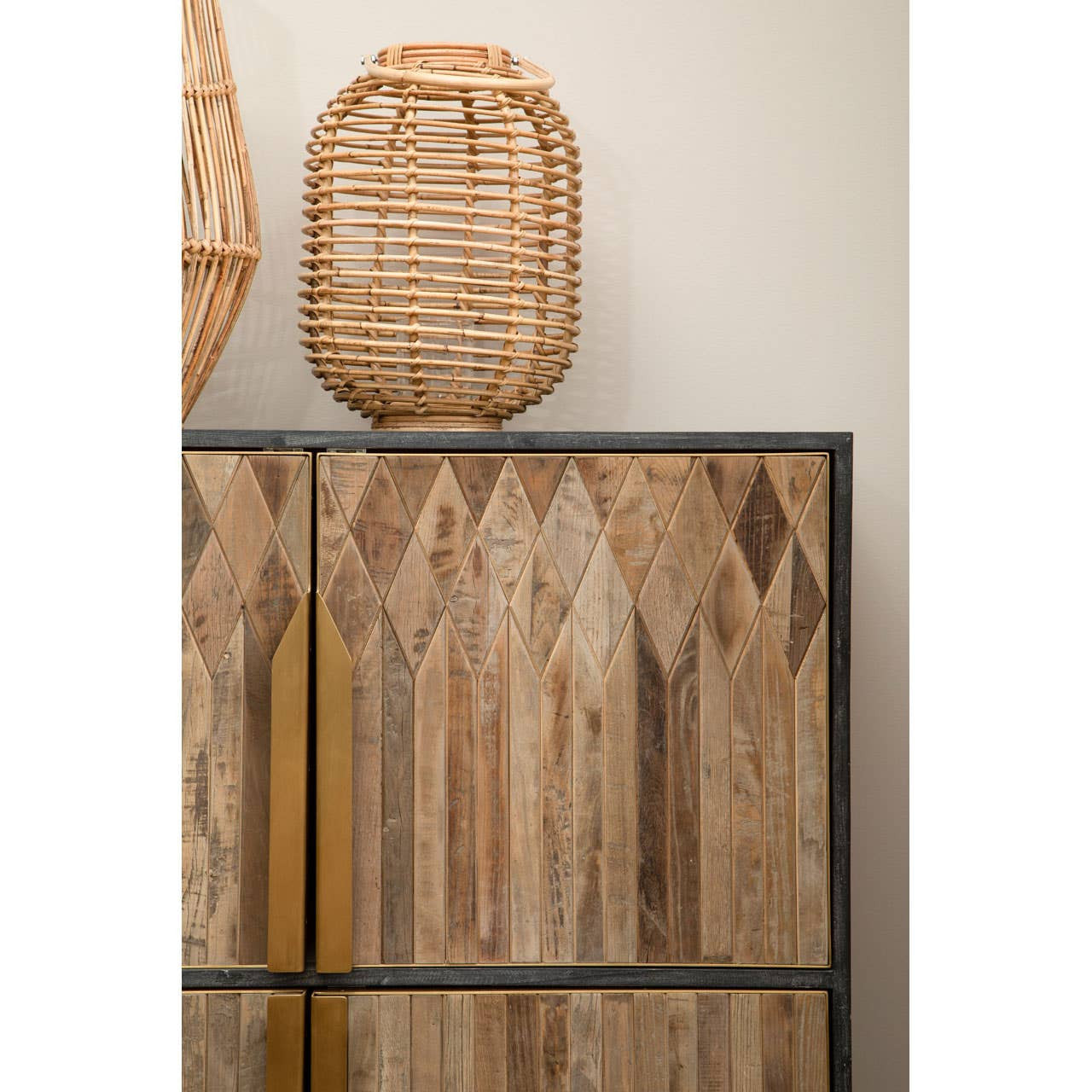 Textured wooden cabinet featuring a geometric pattern on the doors, with a sleek black frame and gold handles. A woven lantern sits on top, adding a natural element to the decor. The background is a neutral wall, enhancing the cabinet's warm tones