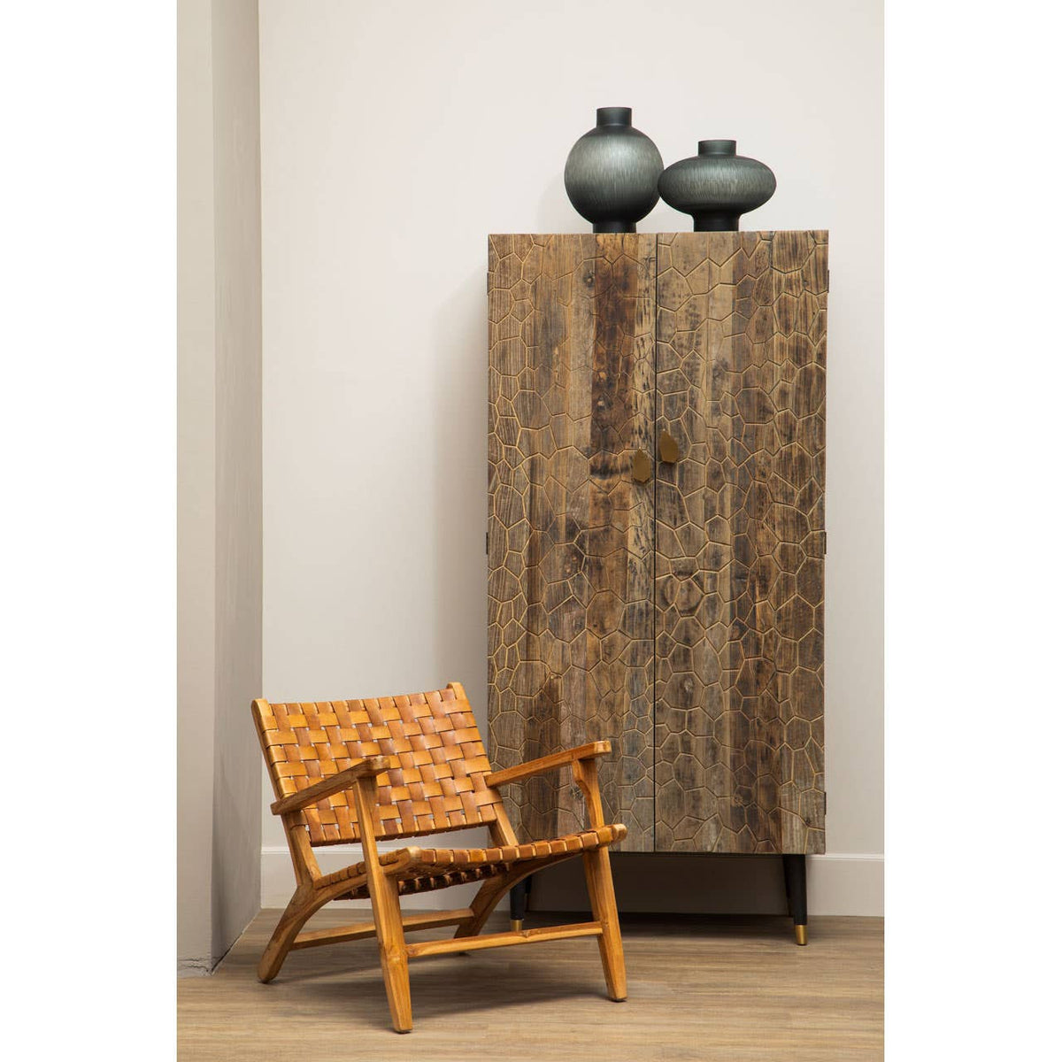 Tall cabinet made of recycled elm wood with a natural finish, featuring two doors and a textured surface. On top of the cabinet, there are two dark ceramic vases. Next to the cabinet, there is a light wooden chair with a woven seat and backrest, placed on a light-colored floor against a neutral wall
