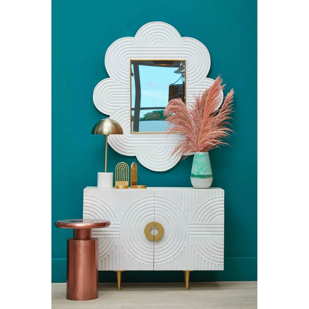 White textured sideboard with gold legs, decorative mirror, table lamp, and vase display