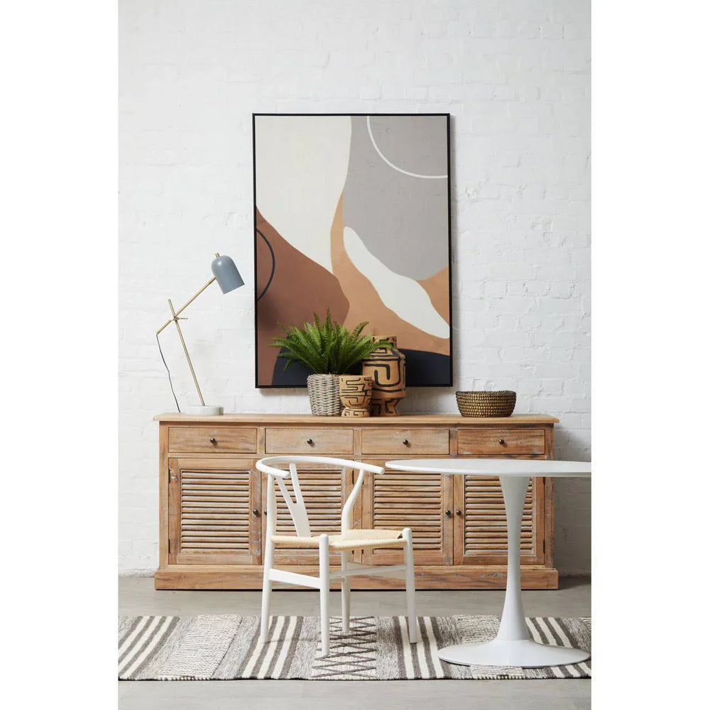 Wood sideboard with abstract wall art, table, white chair, and indoor plant decor