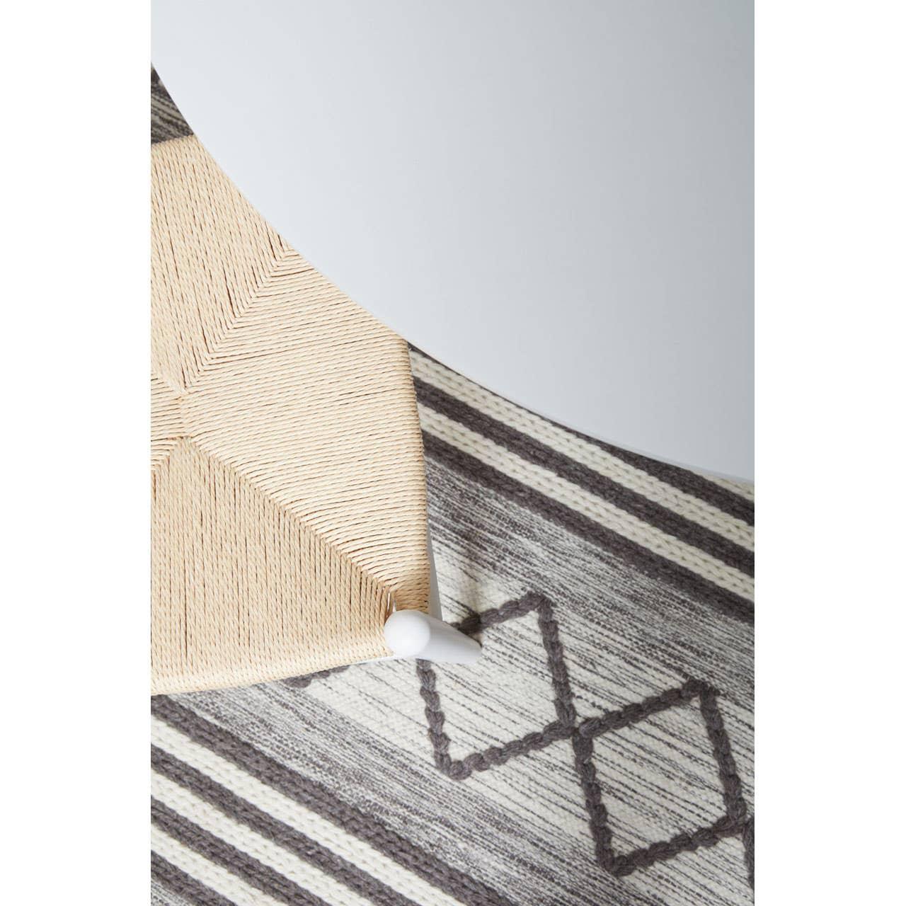 Geometric pattern area rug with grey stripes under white table and woven chair leg