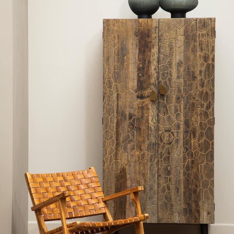 Textured wood cabinet with geometric pattern beside woven leather accent chair on wooden floor