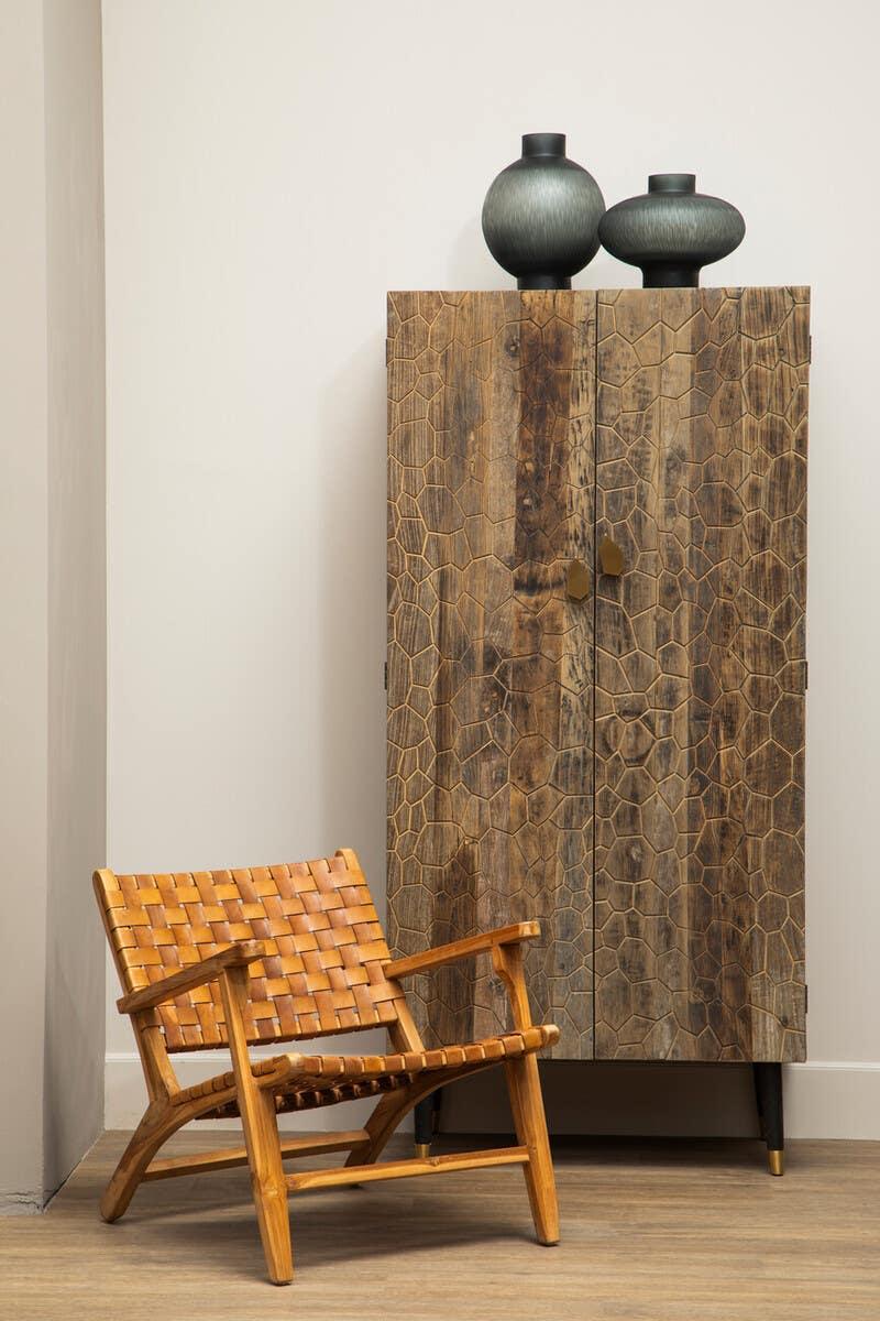 Textured wood cabinet with geometric pattern beside woven leather accent chair on wooden floor