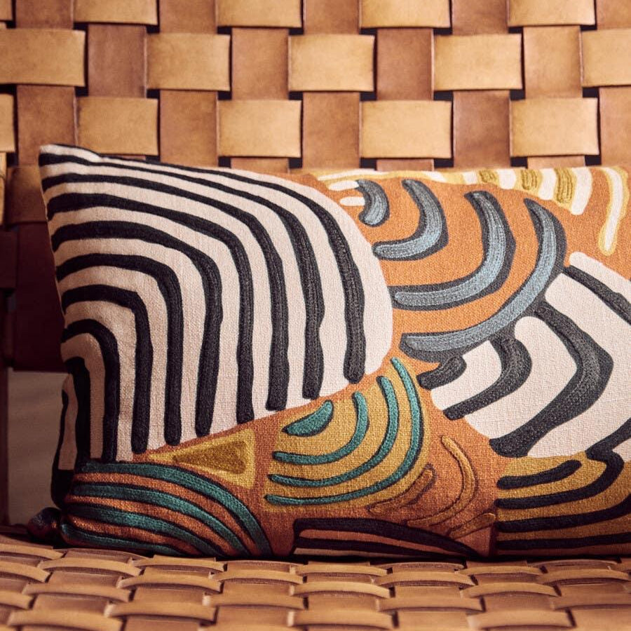 Tan leather woven chair with geometric embroidered cushion in earthy tones