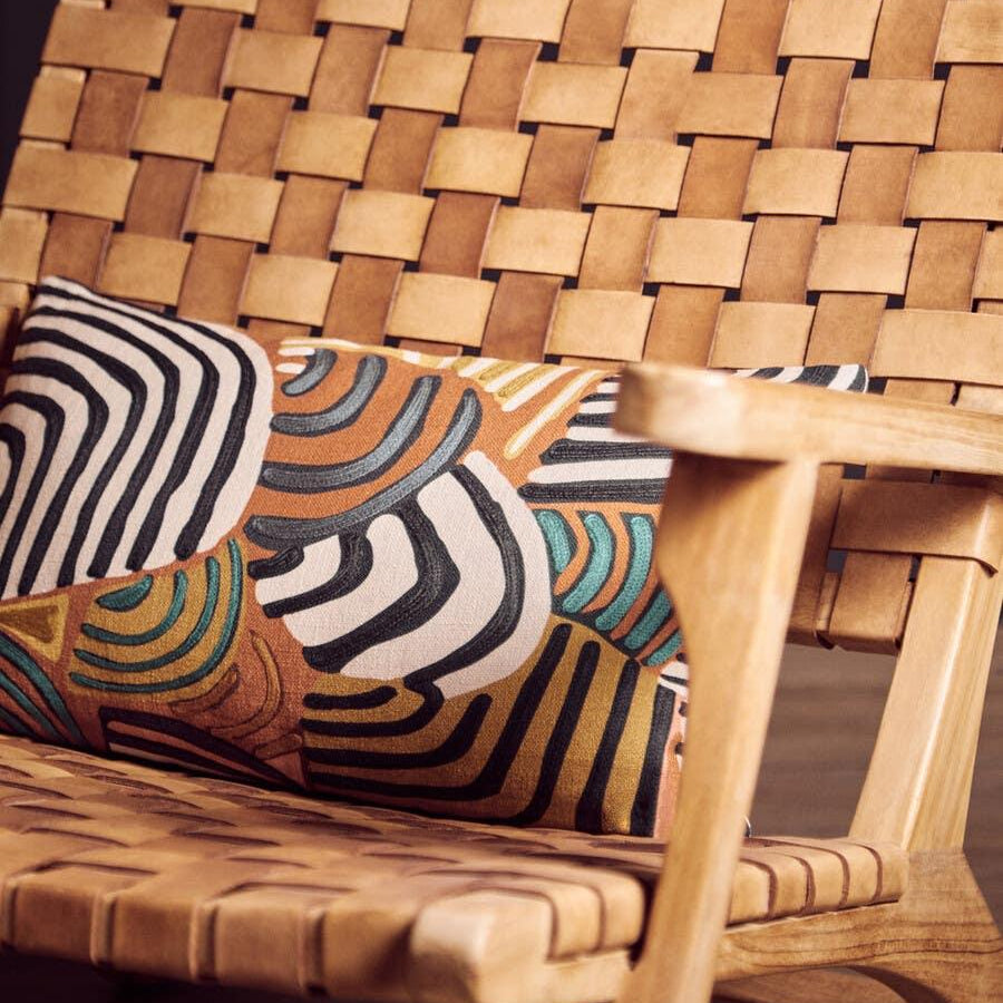 Woven leather armchair with geometric cushion on wooden floor