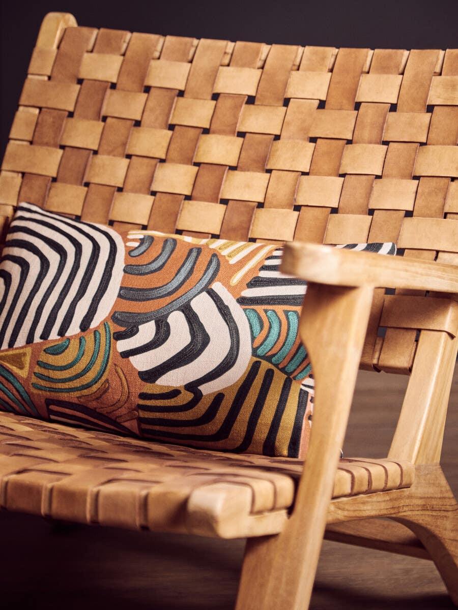 Woven leather armchair with geometric cushion on wooden floor
