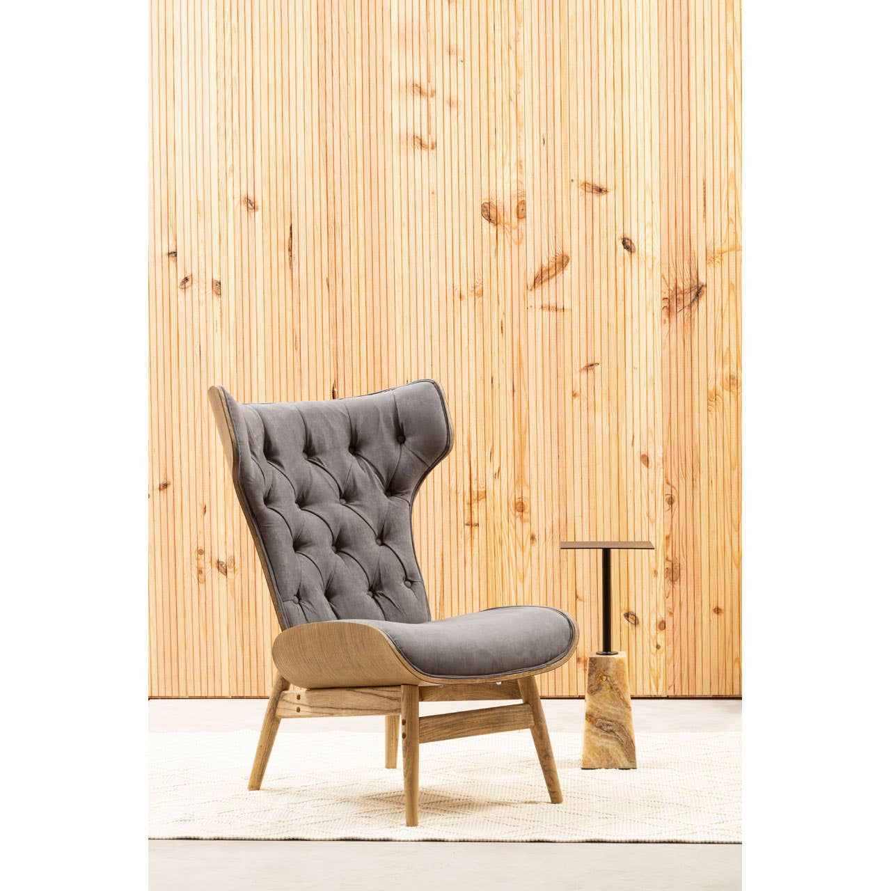 Dark grey velvet chair featuring a winged back and tufted upholstery, set against a backdrop of vertical wooden slats.
