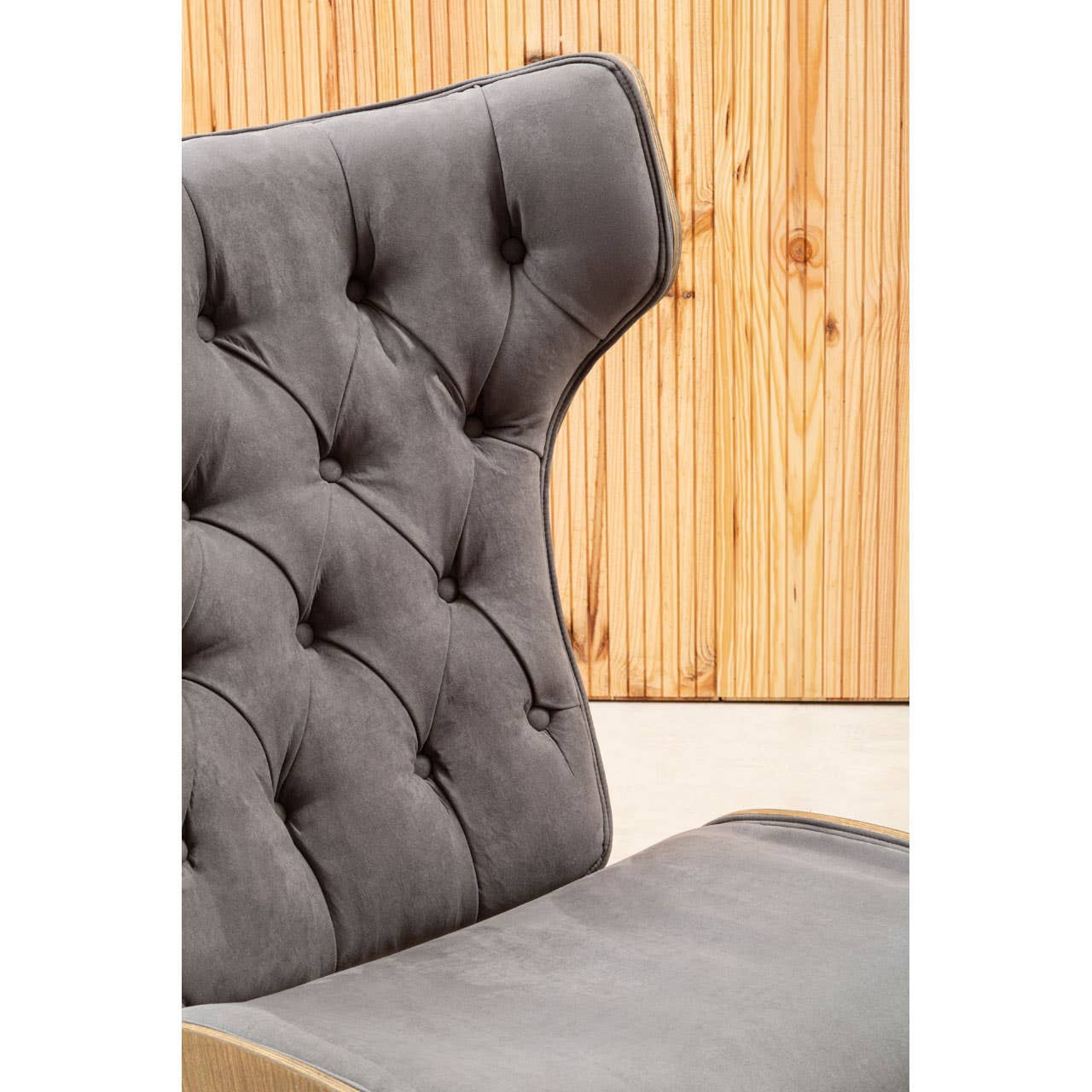 Dark grey velvet chair featuring a winged back design with tufted detailing and button accents. The plush upholstery is complemented by a smooth, curved seat.