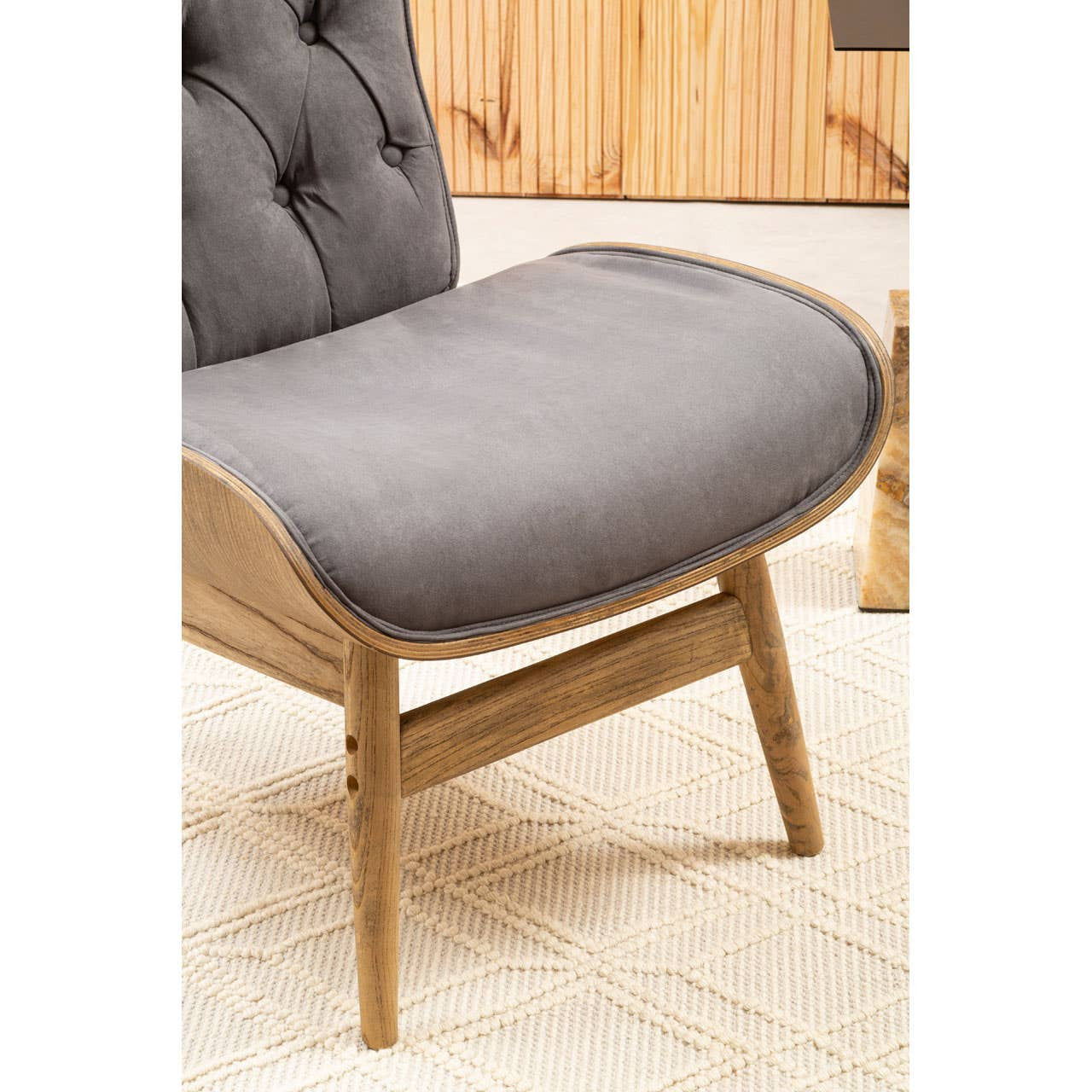 Dark grey velvet chair featuring a winged back and tufted detailing, supported by sturdy wooden legs. The seat is plush and curved for comfort, set against a textured cream rug.