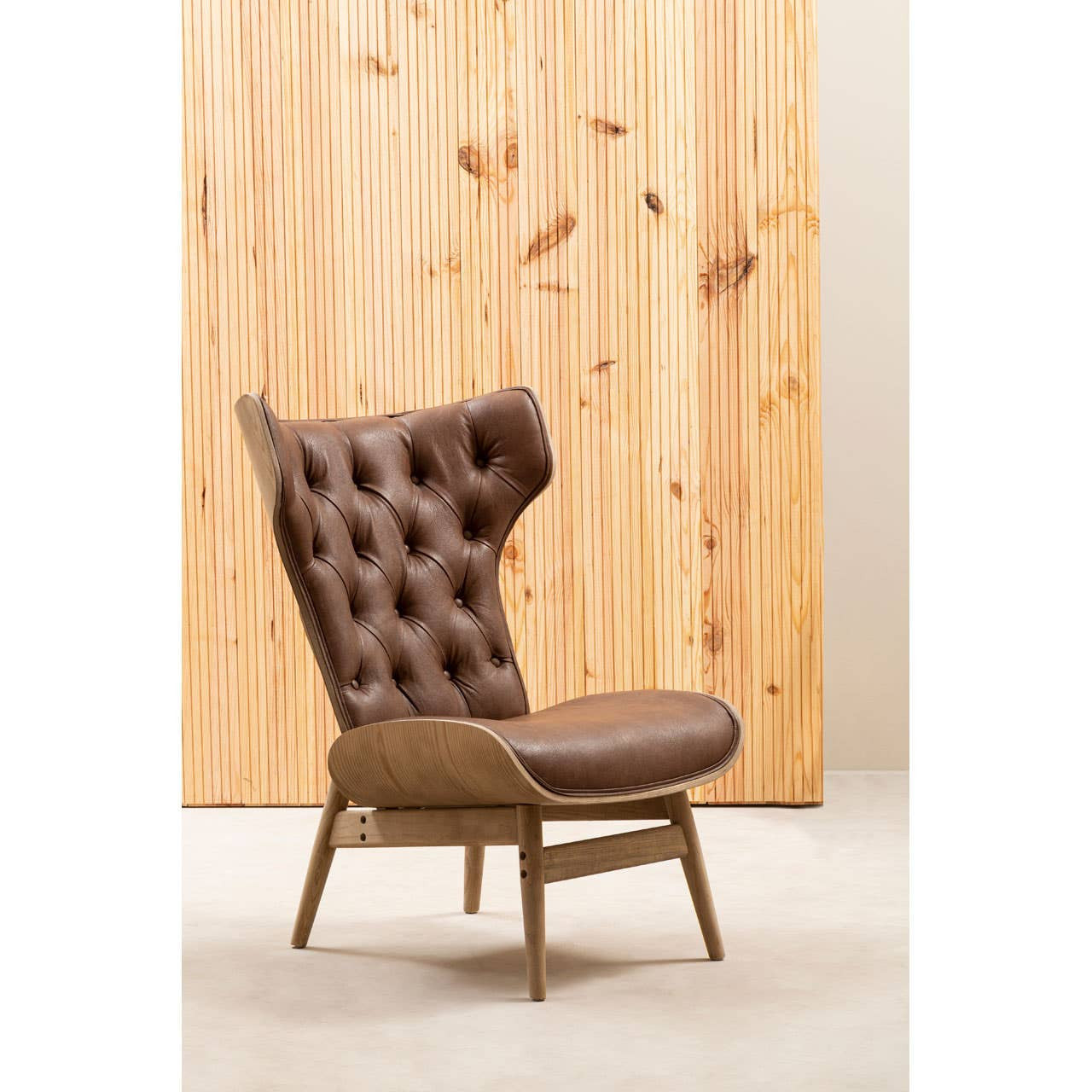 Brown leather effect chair featuring a winged back and tufted upholstery, supported by a light wood frame with angled legs.
