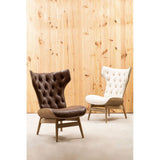 Brown leather effect chair featuring a winged back and tufted upholstery, set against a textured wooden wall.