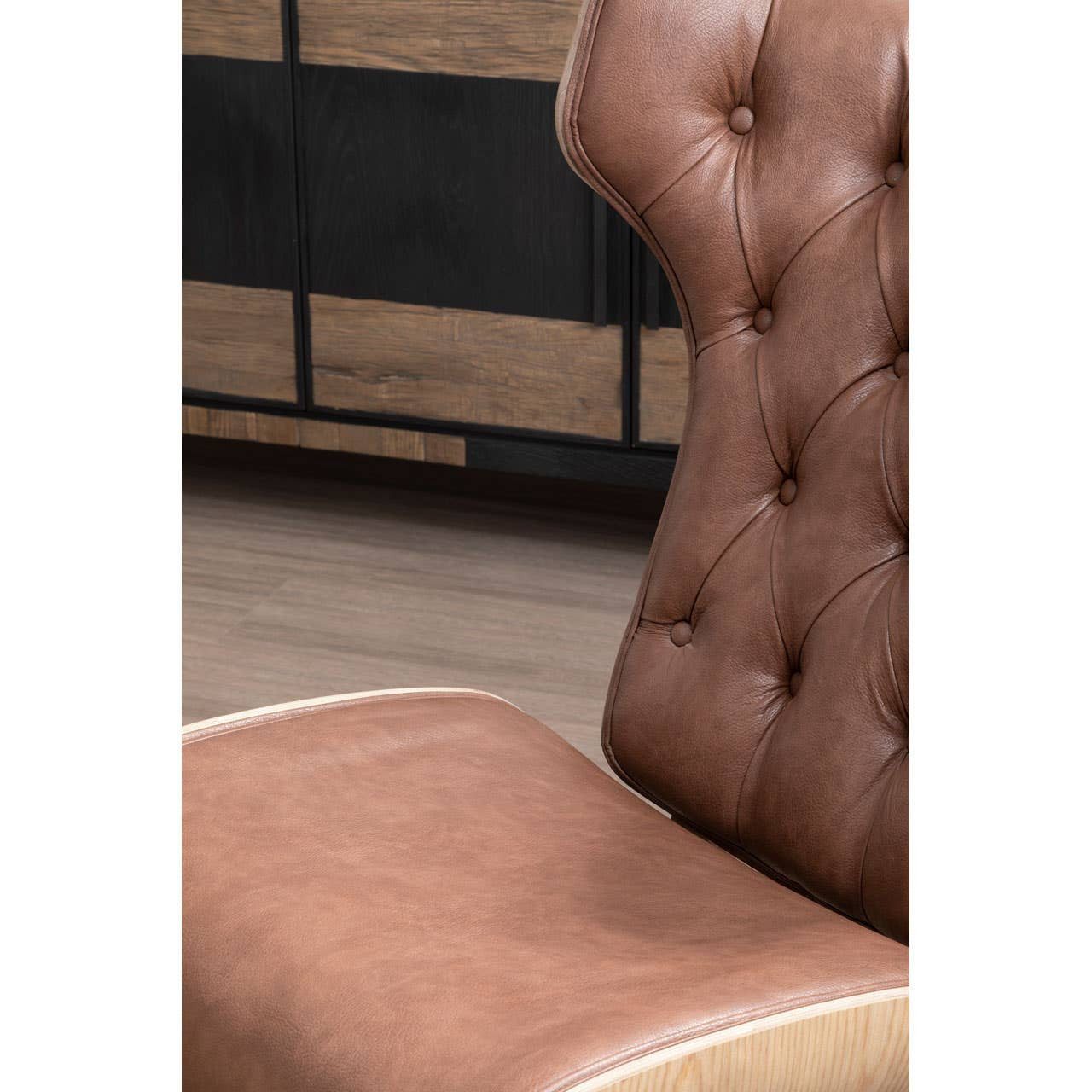 Brown leather effect chair featuring a winged back design with tufted detailing. The seat is cushioned for comfort, and the chair has a smooth finish with a light wood trim.