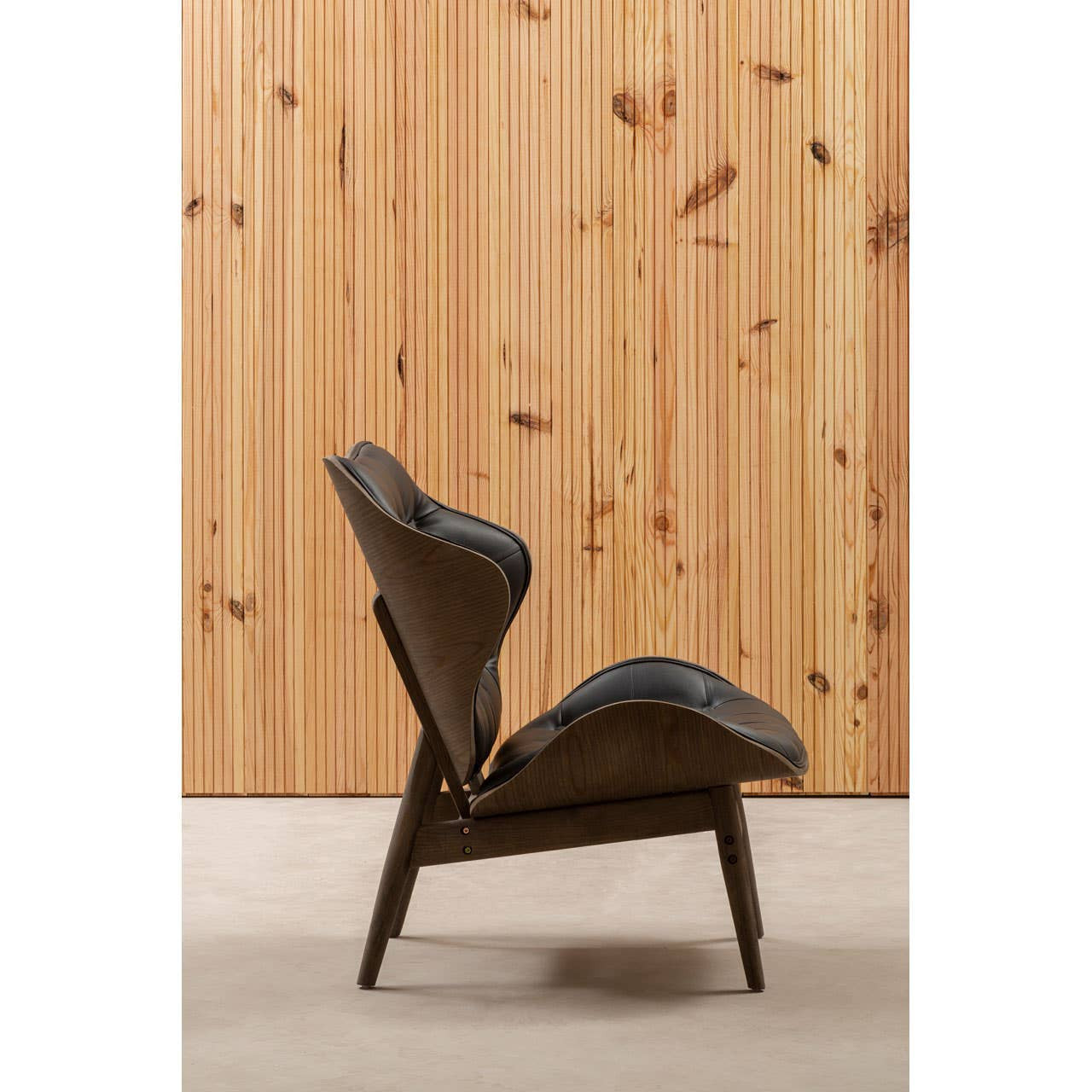 Stylish black leather effect chair featuring a curved design and plush cushioning, set against a backdrop of vertical wooden paneling.